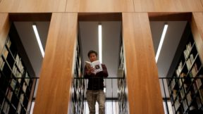 Ein Student steht in einer Bibliothek und liest ein Buch.
